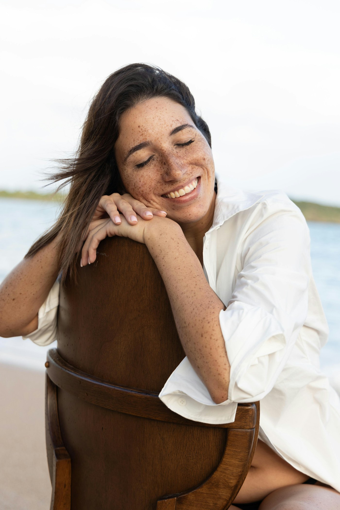 Smiling woman in a white shirt resting on a chair by the sea